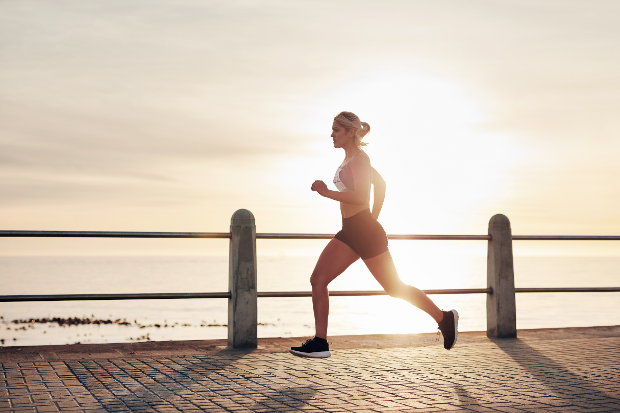 Vrouw die hardloopt langs het water bij zonsondergang, sportieve hardlooptraining in de stad
